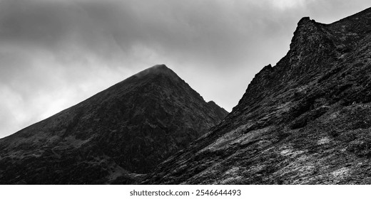 A striking mountain landscape features sharp peaks and rocky slopes under a cloudy sky. The black and white contrast highlights the rugged terrain, emphasizing the natural beauty. - Powered by Shutterstock