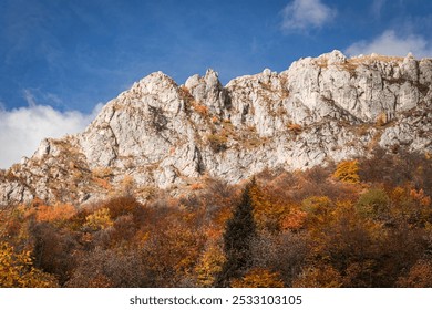 Striking mountain landscape with rocky cliffs and autumn trees below. The clear blue sky and the bright colors of the leaves make for a dramatic and picturesque view - Powered by Shutterstock