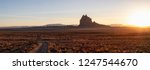 Striking panoramic landscape view of a dirt road in the dry desert with a mountain peak in the background during a vibrant sunset. Taken at Shiprock, New Mexico, United States.