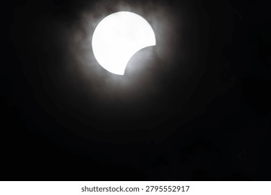 A striking partial solar eclipse with the sun partially obscured by the moon, surrounded by a halo of clouds.