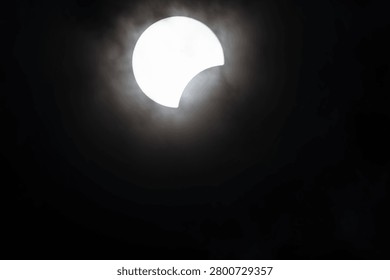 A striking partial solar eclipse with the sun partially obscured by the moon, surrounded by a halo of clouds.