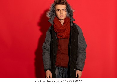 Striking pose! A stylish guy in a jacket stands out against a vibrant red backdrop, creating a captivating image with bold contrast.