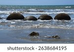 A striking view of the famous Moeraki Boulders partially submerged in ocean water at Koekohe Beach, New Zealand. Captured in November, this image showcases the unique spherical rock formations.