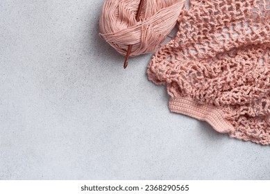 String bag in the process of knitting. Delicate pink mesh bag, crochet hook and remaining yarn. Reusable shopping bags. 