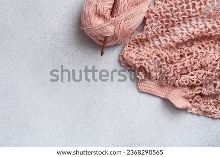 String bag in the process of knitting. Delicate pink mesh bag, crochet hook and remaining yarn. Reusable shopping bags. 