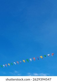 A string of colorful triangular flags flutters against a clear blue sky, evoking a festive and cheerful atmosphere perfect for an outdoor celebration or community event.