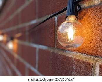 A string of decorative LED bulbs lit up and glowing against a red brick wall