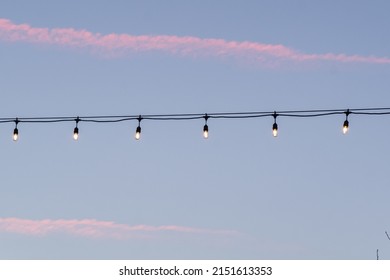 String Of Edison Lightbulbs At Sunset With Sky In Background