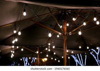 String Of Light Bulb Lamps Suspended From A Sunshade On The Backyard Terrace Night Lighting Is Warm Illuminations Close Up, Nobody.