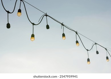 string of light bulbs hanging against a clear sky. The light bulbs are evenly spaced along the wire, which is slightly curved between the points where it is attached.