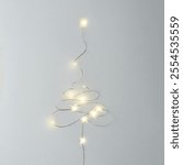 String lights arranged in the shape of a Christmas tree on a light background. A minimalist and modern composition creating a festive mood and a sense of lightness