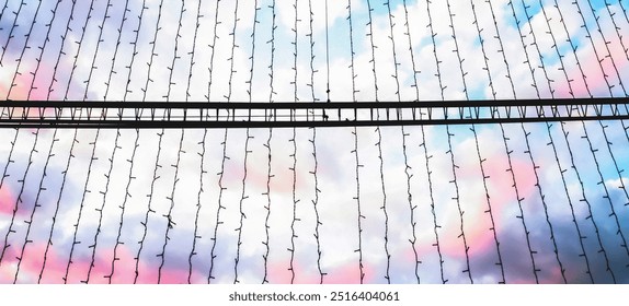 String lights hang against a backdrop of pastel-colored clouds during sunset. The soft colors and delicate lights create a dreamy, peaceful mood. Dreaminess, atmospheric contrast, festive concept