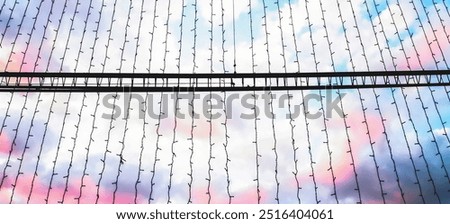String lights hang against a backdrop of pastel-colored clouds during sunset. The soft colors and delicate lights create a dreamy, peaceful mood. Dreaminess, atmospheric contrast, festive concept