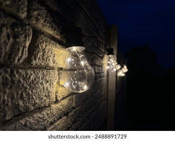 String lights hanging on a textured brick wall during nighttime. The warm glow of the lights contrasts beautifully with the dark blue sky, creating a cozy and inviting atmosphere. - Powered by Shutterstock