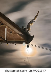 A string of lights hangs below the roof's edge, with one bulb glowing brightly and casting a strong, circular flare of light. The night sky above is filled with soft, textured clouds, creating a drama