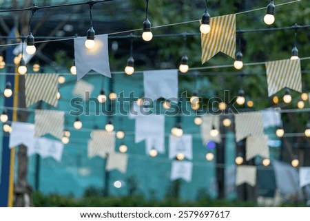 A string of lights with white and yellow flags hanging from them. The lights and flags create a festive and celebratory atmosphere