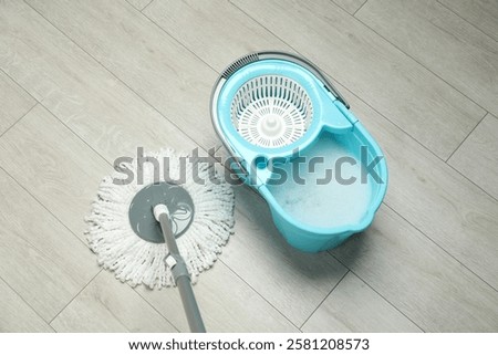 String mop and bucket with detergent on wooden floor, above view