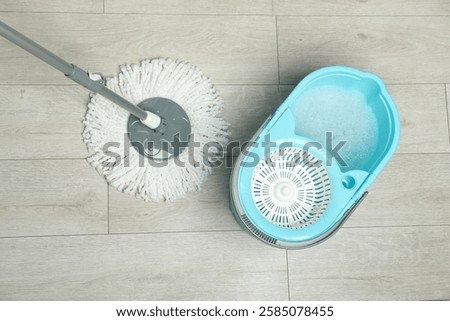 String mop and bucket with detergent on wooden floor, top view