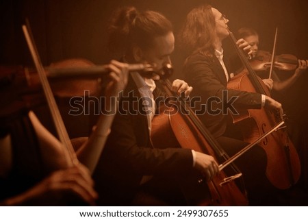 String quartet passionately playing cellos and violins while sitting in row on stage in misty orange light, copy space