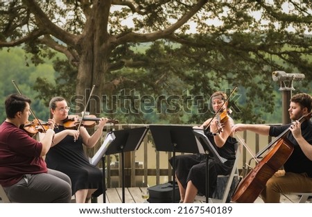 String quartet of two young men and two young women playing concert on wooden deck above Missouri River on summer evening