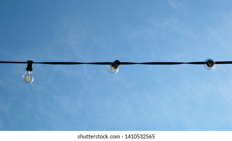 A string wire of outdoor light bulbs hanging against a clear blue sky. Light bulbs on the sky background. Panoramic view.
