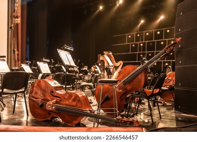stringed musical instruments of the symphony orchestra lie on the stage before the concert rehearsal. Violins cellos double basses on an empty stage - Shutterstock ID 2266546457