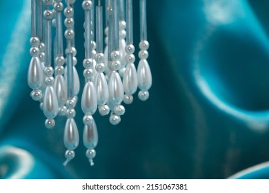 Strings of beaded accents for wedding or formal wear with faux pearl and teardrop beads, suspended in front of a turquoise satin fabric backdrop.