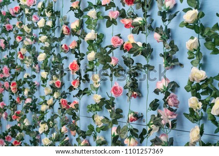 Strings of pink and white artificial roses hanging against a wall painted baby blue.