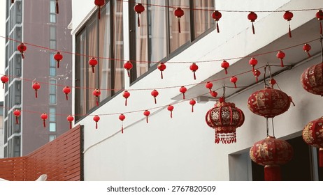 Strings of small red lanterns and larger ornate lanterns decorate a white city building.
