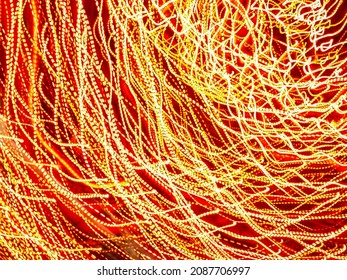 Stringy overlapping light trails of glowing LEDs at a holiday celebration in an ornamental garden at night. Long exposure with motion blur. Light painting.