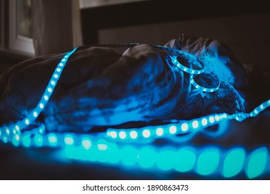 A Strip Blue Colored Strip Led Neon Light Shining On A Messy Bed With Quilt In A Dark Bedroom In Front Of A Window And Curtain