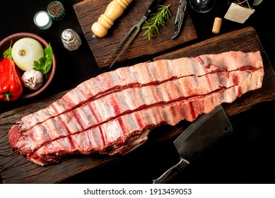 Strip Of Roast Beef, Fresh Beef Ribs, On Wooden Board With Vegetables And Rotisserie Knife With Pepper Mortar And Knife And Fork.