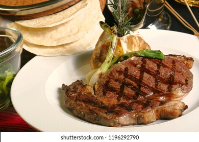 Strip Steak Grilled Accompanied By Cambray Onions And Baked Potato. The Strip Steak Is A Cut Of Beef Steaks From The Short Loin From A Cow.