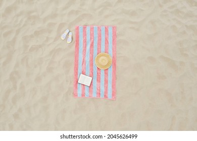 Striped Beach Towel, Book, Straw Hat And Flip Flops On Sand, Aerial View