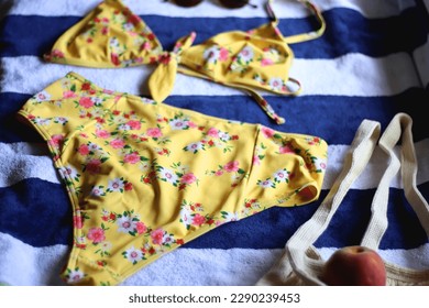 Striped beach towel, floral yellow swimsuit, sunglasses and mesh bag with peaches. Cute beach essentials. Selective focus. - Powered by Shutterstock