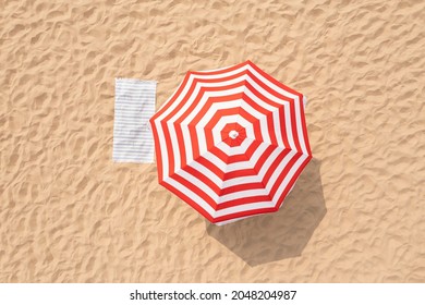 Striped beach umbrella near towel on sand, aerial view