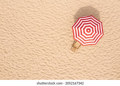 Striped beach umbrella near wooden sunbed on sandy coast, aerial view. Space for text