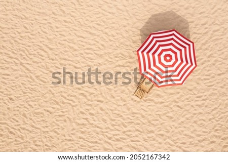 Striped beach umbrella near wooden sunbed on sandy coast, aerial view. Space for text