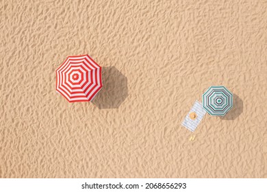 Striped Beach Umbrellas, Towel, Hat And Flip Flops On Sandy Coast, Aerial View