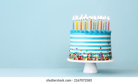 Striped buttercream birthday cake with colorful birthday candles and sprinkles on a blue background