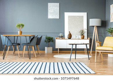 Striped carpet in grey apartment interior with chairs at dining table and paintings on the wall