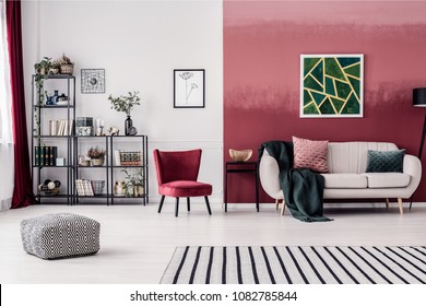 Striped Carpet And Pouf In Spacious Living Room Interior With Red Armchair And Green Painting