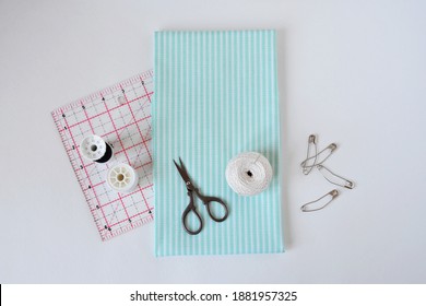 Striped Cotton Fabric, Small Scissors, Threads, Needle, Quilting Ruler And Pins Over White
