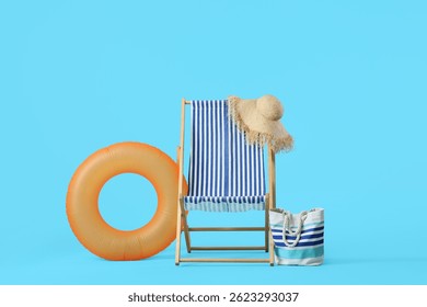 Silla de cubierta rayada con el anillo inflable, sombrero de mimbre y bolso de la playa en fondo azul