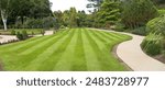 Striped lawn with trees, paths and arch in large garden.