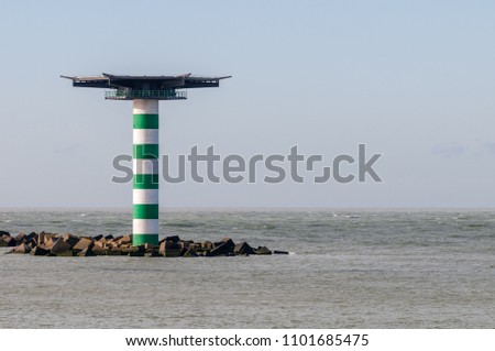 The striped lighthouse Maasmond with heliplatform at the entrance of the Port of Rotterdam in the Netherlands. The lighthouse is situated at the end of pier Zuiderdam with concrete wave breakers.
