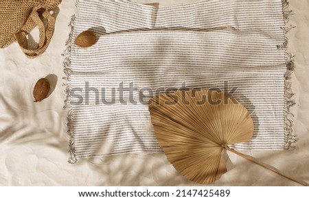 Striped linen beach towel, woven bag and two coconuts on sandy beach with shadows from palm tree. Relaxation and tropical summer holidays concept