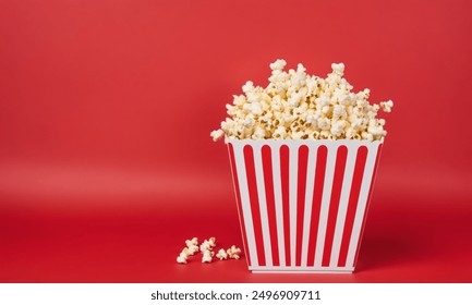 Striped popcorn bucket with popcorn on red background