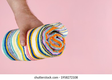 Striped Towel And Hand On A Pink Background. Man Holding A Multi-colored Towel Rolled Up. Side View. Selective Focus.