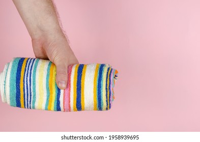 Striped Towel And Hand On A Pink Background. Man Holding A Multi-colored Towel Rolled Up. Side View. Selective Focus.